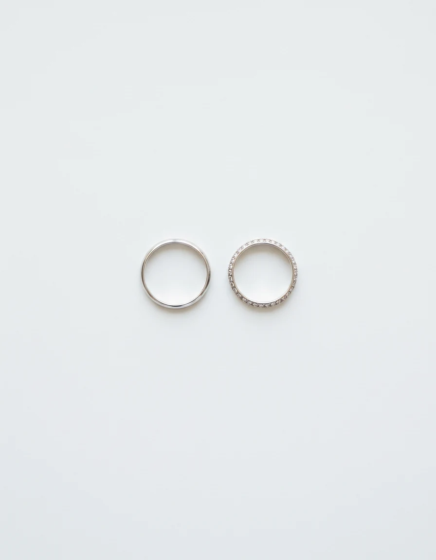 Two platinum wedding bands lying side by side, one plain and one pave-set.