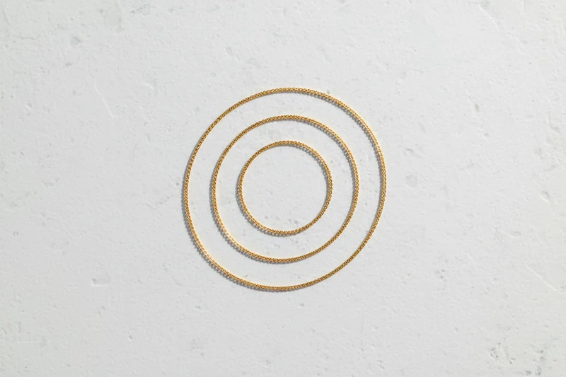 A fine gold chain coiled loosely on pale limestone.