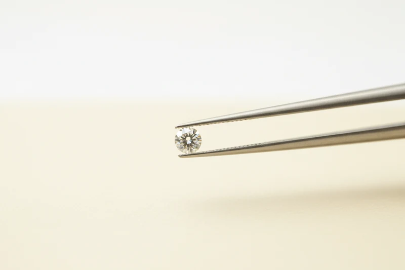 Tweezers holding a single loose round brilliant-cut diamond.